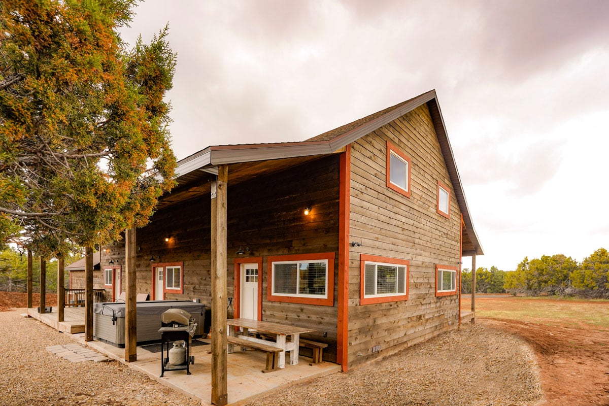 A modern wooden cabin with a covered porch and outdoor seating in a rural setting.